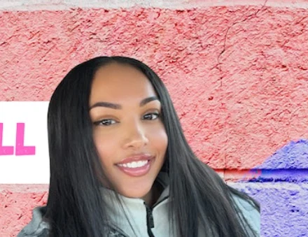 Briana Bull, host of The Know Bull Podcast, smiling in front of a pink painted wall